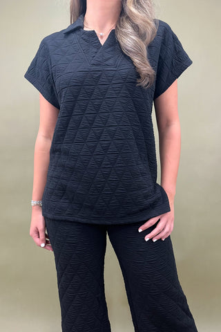 Person wearing a black textured top and pants against a beige background