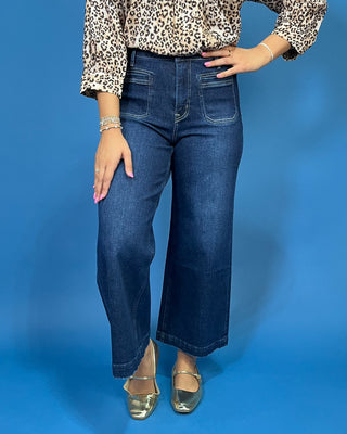 A person wearing dark blue wide-leg cropped jeans, a leopard-print blouse, and metallic gold flats