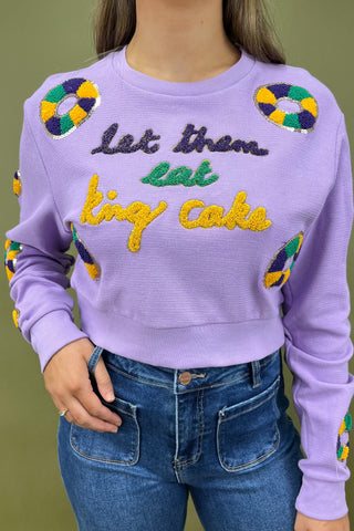 Person wearing a purple sweater with colorful text and designs, standing against a green background.