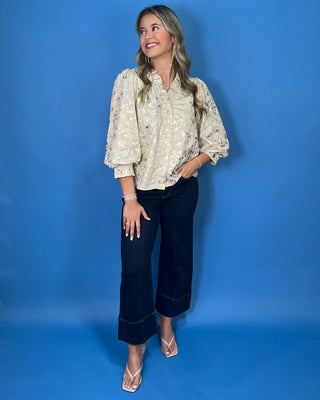 Ivory metallic blouse with abstract shimmer, ruffled V-neckline, button front, and puff sleeves.