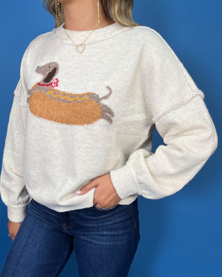 Ivory knit sweater with long sleeves, relaxed fit and a playful dachshund hot dog graphic.