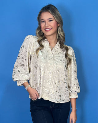 Ivory metallic blouse with abstract shimmer, ruffled V-neckline, button front, and puff sleeves.
