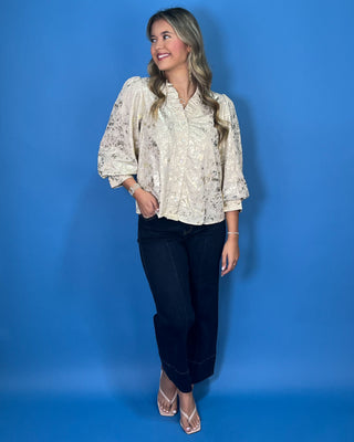 Ivory metallic blouse with abstract shimmer, ruffled V-neckline, button front, and puff sleeves.
