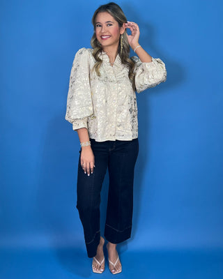 Ivory metallic blouse with abstract shimmer, ruffled V-neckline, button front, and puff sleeves.