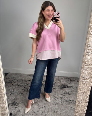 Woman taking a mirror selfie wearing a pink top and blue jeans.