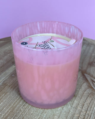 Pink candle in a glass container on a wooden surface with a pink background