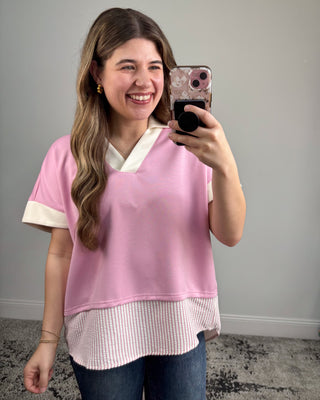 Woman taking a mirror selfie wearing a pink and white layered top.