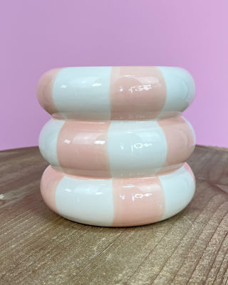 Stack of pink and white striped cylindrical objects on a wooden surface with a pink background