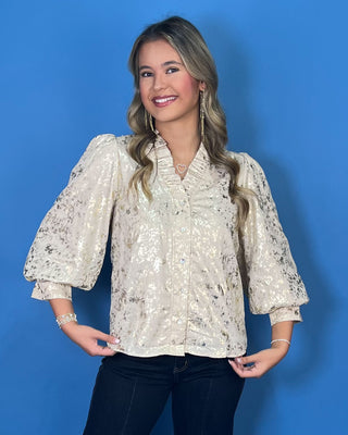 Ivory metallic blouse with abstract shimmer, ruffled V-neckline, button front, and puff sleeves.