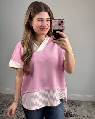 Woman taking a mirror selfie wearing a pink layered top.