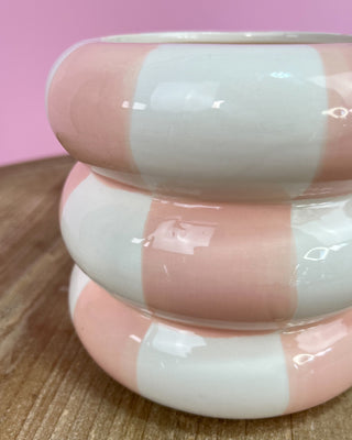 Pink and white striped bangle on a wooden surface with a pink background