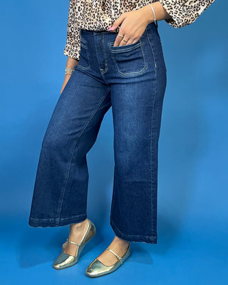 A person wearing dark blue wide-leg cropped denim jeans, a leopard print blouse, and metallic silver flats
