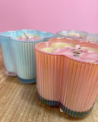 Three scented candles in decorative containers on a wooden surface with a pink background