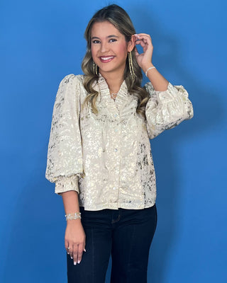 Ivory metallic blouse with abstract shimmer, ruffled V-neckline, button front, and puff sleeves.