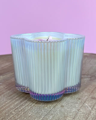 Candle in a ribbed glass container on a wooden surface with a pink background