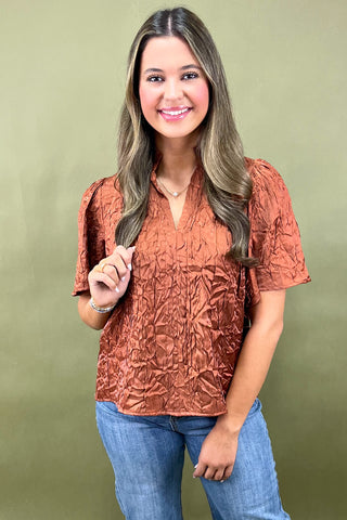 Woman wearing a textured orange top and blue jeans against a green background