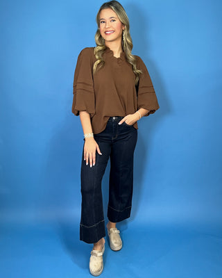 Chocolate brown blouse with a ruffled V-neckline, three-quarter balloon sleeves, and relaxed fit.