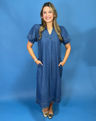 A sleeveless white midi dress with a purple and black floral print, featuring side pockets, worn by a model against a solid pink background.