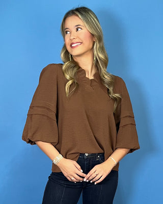 Chocolate brown blouse with a ruffled V-neckline, three-quarter balloon sleeves, and relaxed fit.