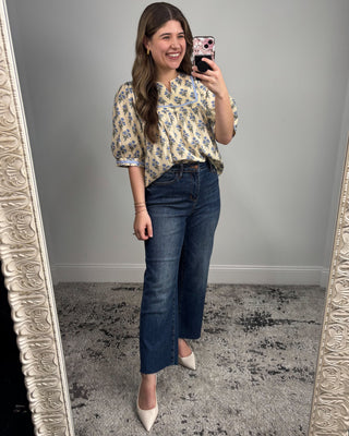 Woman taking a mirror selfie wearing a floral blouse and blue jeans.