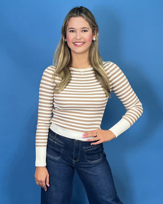 A woman modeling a beige and white horizontally striped long-sleeve knit top with dark wide-leg jeans and metallic gold flats
