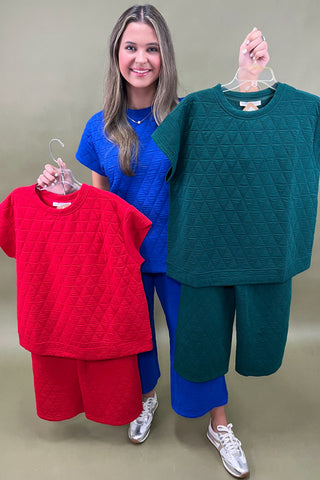Woman holding two hangers with red and green textured shirts against a plain background