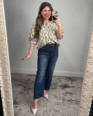 Woman taking a mirror selfie wearing a floral blouse and blue jeans.