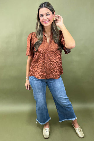 Woman wearing a brown textured top and blue jeans against a green background