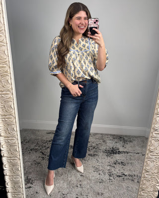 Woman taking a mirror selfie wearing a floral blouse and jeans.