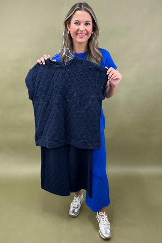 Woman holding a navy blue textured top against a beige background