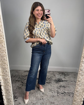 Woman taking a mirror selfie wearing a floral blouse and blue jeans.