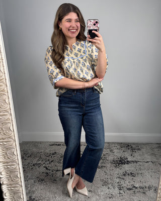 Woman taking a mirror selfie wearing a floral blouse and blue jeans.