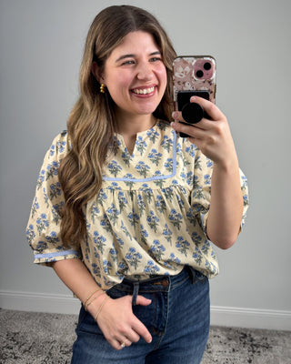 Woman taking a mirror selfie wearing a floral blouse and jeans on a gray background