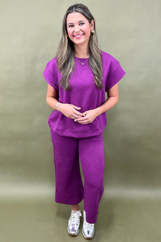 Woman wearing a purple outfit against a plain background