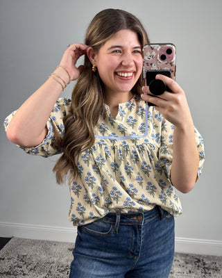 Woman taking a mirror selfie wearing a floral blouse and jeans.