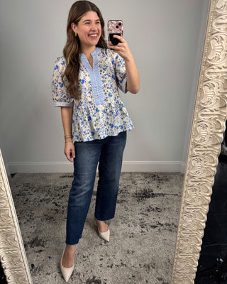 Woman taking a mirror selfie wearing a floral blouse and blue jeans.