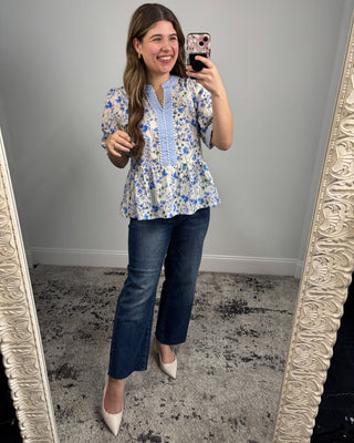 Woman taking a mirror selfie wearing a floral blouse and blue jeans.