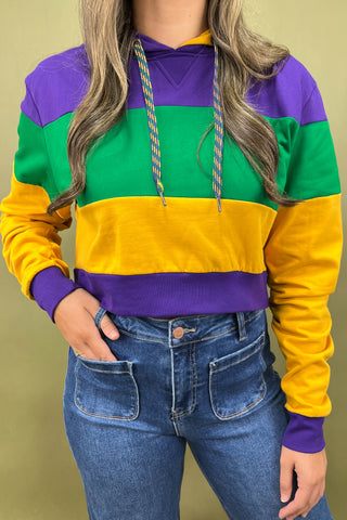 Person wearing a colorful striped hoodie with purple, green, and yellow sections, paired with blue jeans on a beige background.