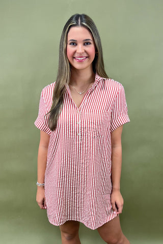 Red and white vertical striped button-down shirt dress with short sleeves and chest pocket, styled casually for a relaxed summer look
