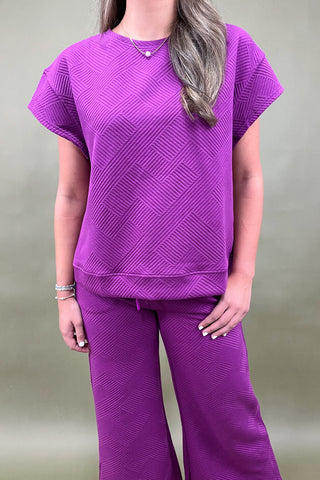 Person wearing a purple textured outfit against a plain background