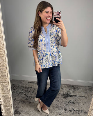 Woman taking a mirror selfie wearing a floral blouse and jeans.