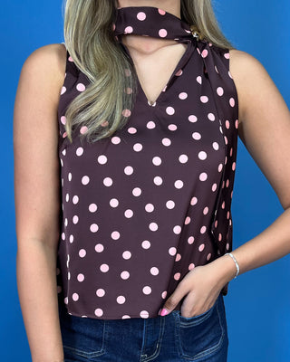 A woman wearing a sleeveless dark brown halter-style top with a pink polka dot pattern, paired with blue jeans