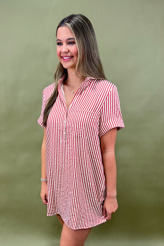Red and white vertical striped button-down shirt dress with short sleeves and chest pocket, styled casually for a relaxed summer look