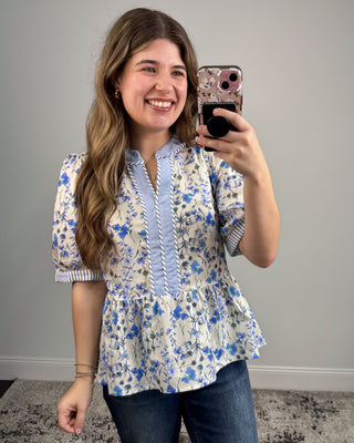 Woman taking a mirror selfie wearing a floral blouse and blue jeans.