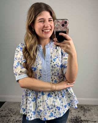 Woman taking a mirror selfie wearing a floral blouse with a plain background