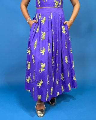 A woman modeling a purple sleeveless dress with yellow tiger prints against a solid blue background.