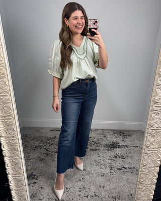 Woman taking a mirror selfie wearing a green striped shirt and blue jeans.