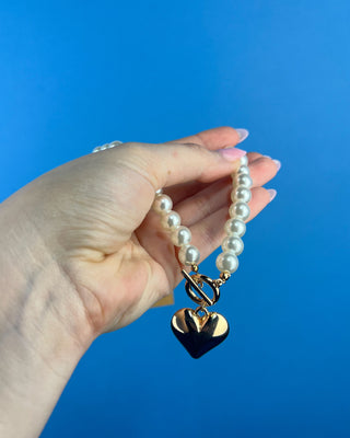Shop the Heart Charm Pearl Necklace featuring classic faux pearls, a gold heart charm, and a stylish toggle clasp for timeless elegance.