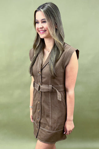 Woman wearing a brown vest over a dress against a green background