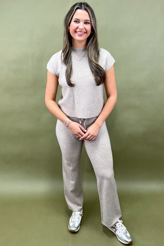 Woman wearing a gray outfit with white sneakers against a green background